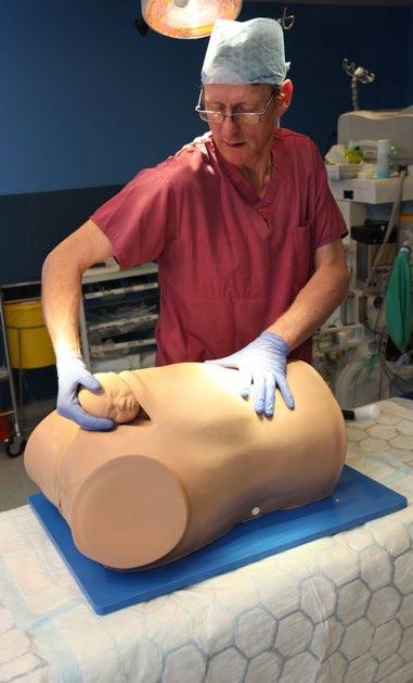 Medical professional demonstrating a procedure on a medical training mannequin in a surgical setting.