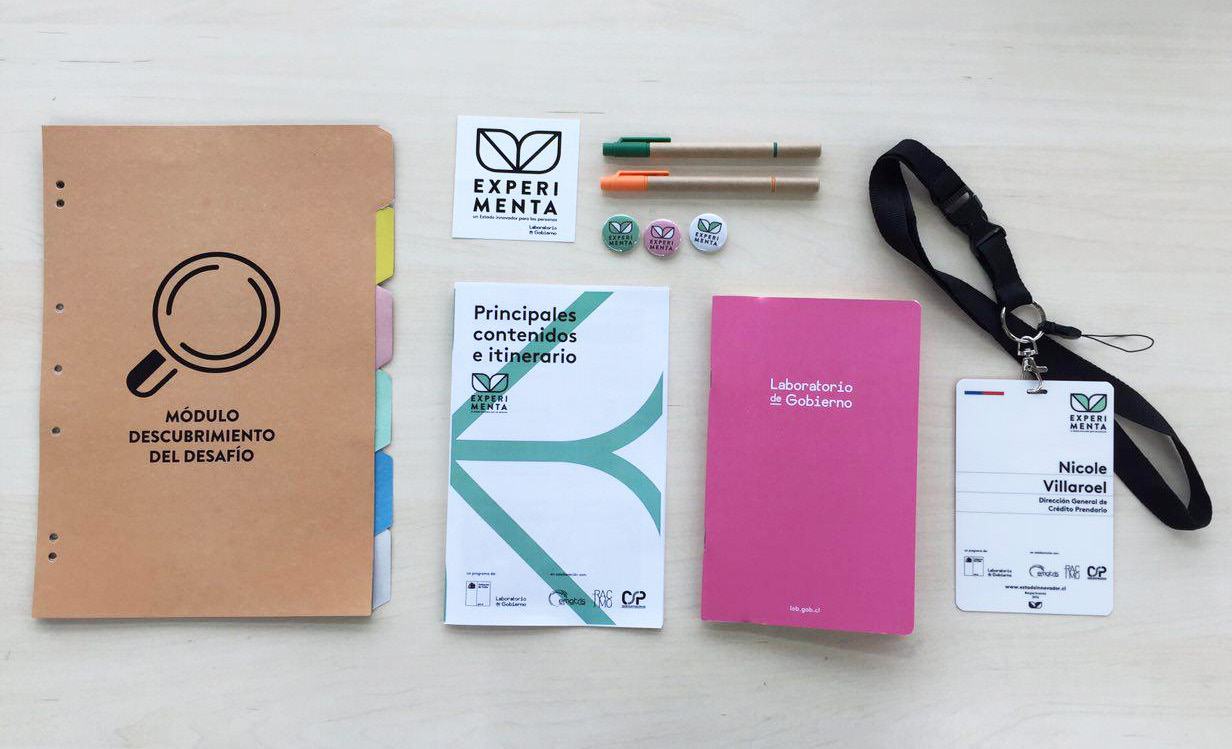 Workshop materials on a table, including branded folders, booklets, pens, pins, and an ID badge for "Nicole Villaroel" from Experimenta.