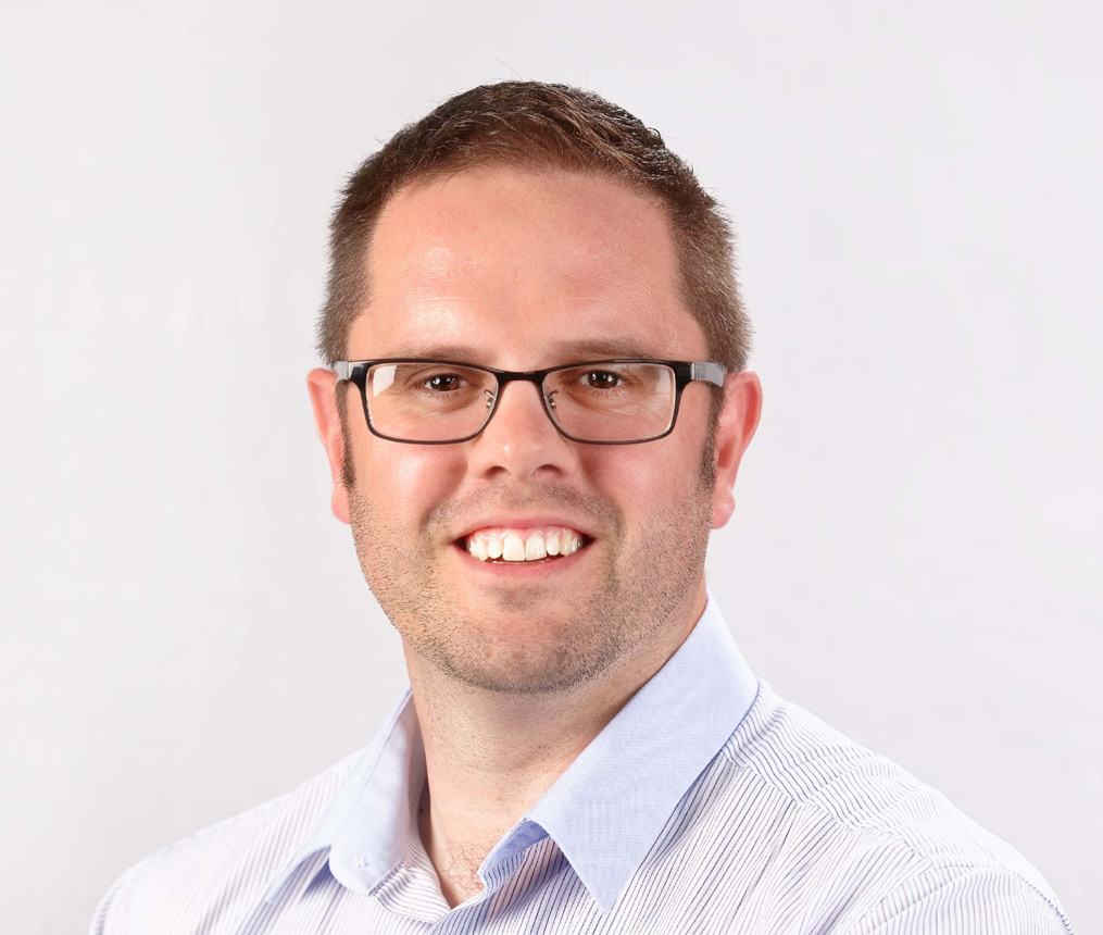 Headshot of a smiling man with glasses and a striped shirt against a plain background.
