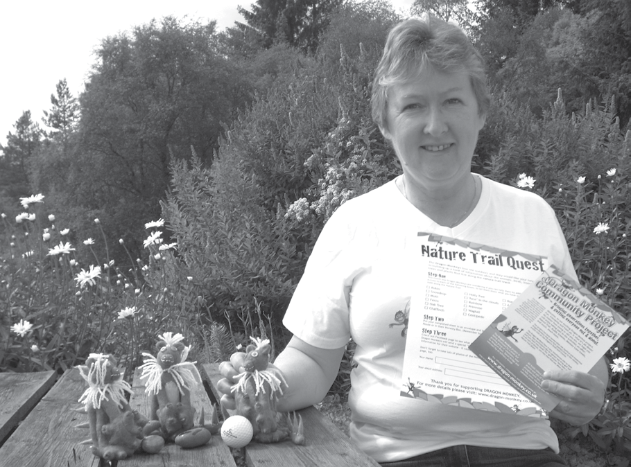 Woman outdoors holding flyers for a "Nature Trail Quest" and "Dragon Monkey Community Project," illustrating educational materials.