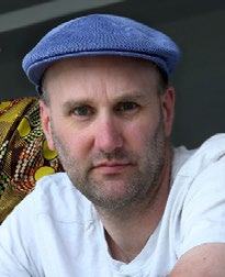 Headshot of a man with short brown hair, beard, and a blue flat cap