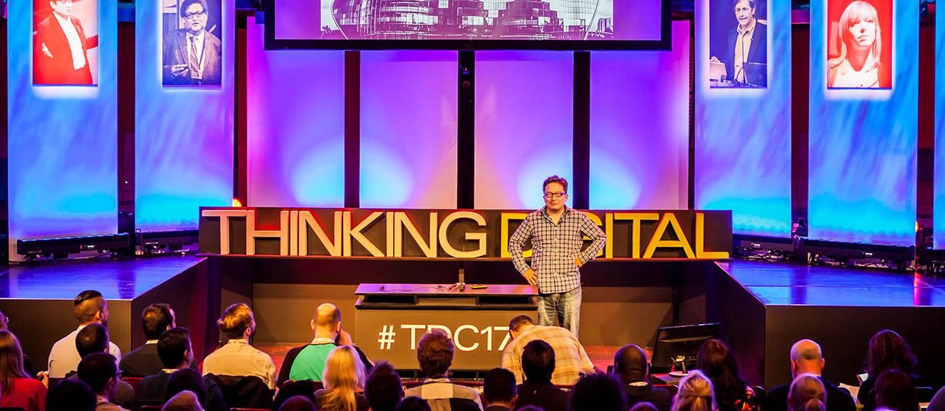 A speaker presents on a large stage with "THINKING DIGITAL" displayed, to an audience at a conference or event.