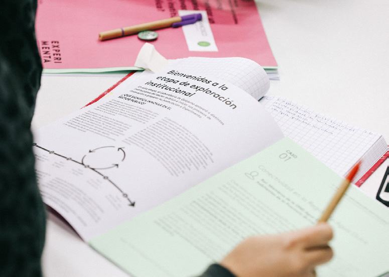 Open workshop booklet showing "Bienvenidos a la etapa de exploración institucional" text and a diagram illustrating a conceptual model with arrows and circles.