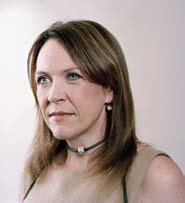 Portrait of a woman with long brown hair looking to the side, wearing a beige top and a dark choker necklace.