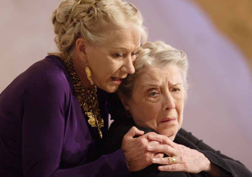 An actress in a purple dress comforts another distressed older woman, embracing her on a stage.