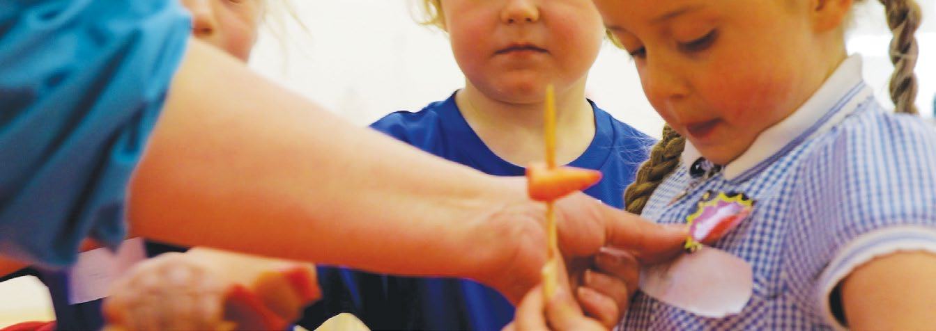 An adult's hand assists a young child with a craft activity involving a stick and paper, illustrating hands-on learning.
