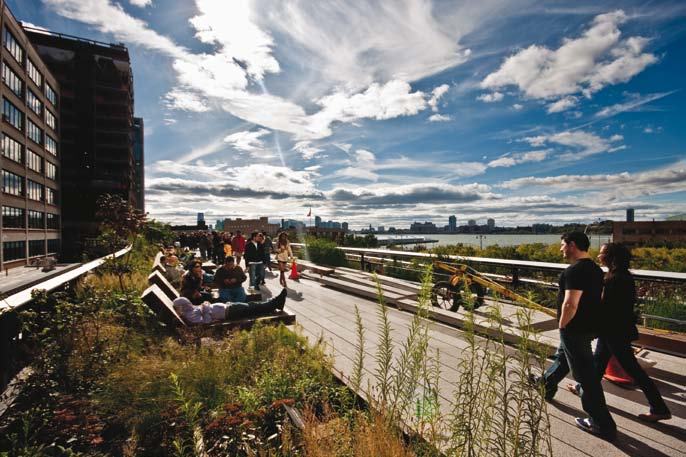 People walking and relaxing on an elevated park with lush greenery and city buildings in the background.