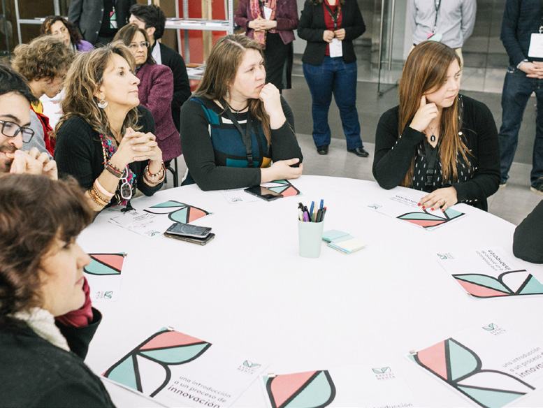 Close-up of several women actively listening and participating at a round table during a workshop, with branded papers in front of them.