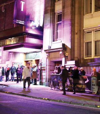 People queuing outside the Glasgow Film Festival in front of a building illuminated with purple lights at night.