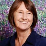 Headshot of a smiling woman with short brown hair against a blurry floral background.