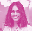 Portrait of a woman with long dark wavy hair and glasses, wearing a light-colored shirt, smiling.