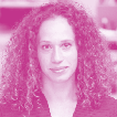 Portrait of a woman with dark curly hair, wearing a dark top, looking ahead.