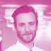 Headshot of a man with a beard and dark hair smiling, tinted pink.