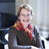 Headshot of a smiling woman with glasses and a colorful scarf, sitting in an indoor setting.