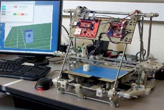 A desktop 3D printer with a small white object on its bed, next to a computer displaying a 3D modeling software interface.