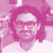 Headshot of a man with long dark curly hair and glasses.