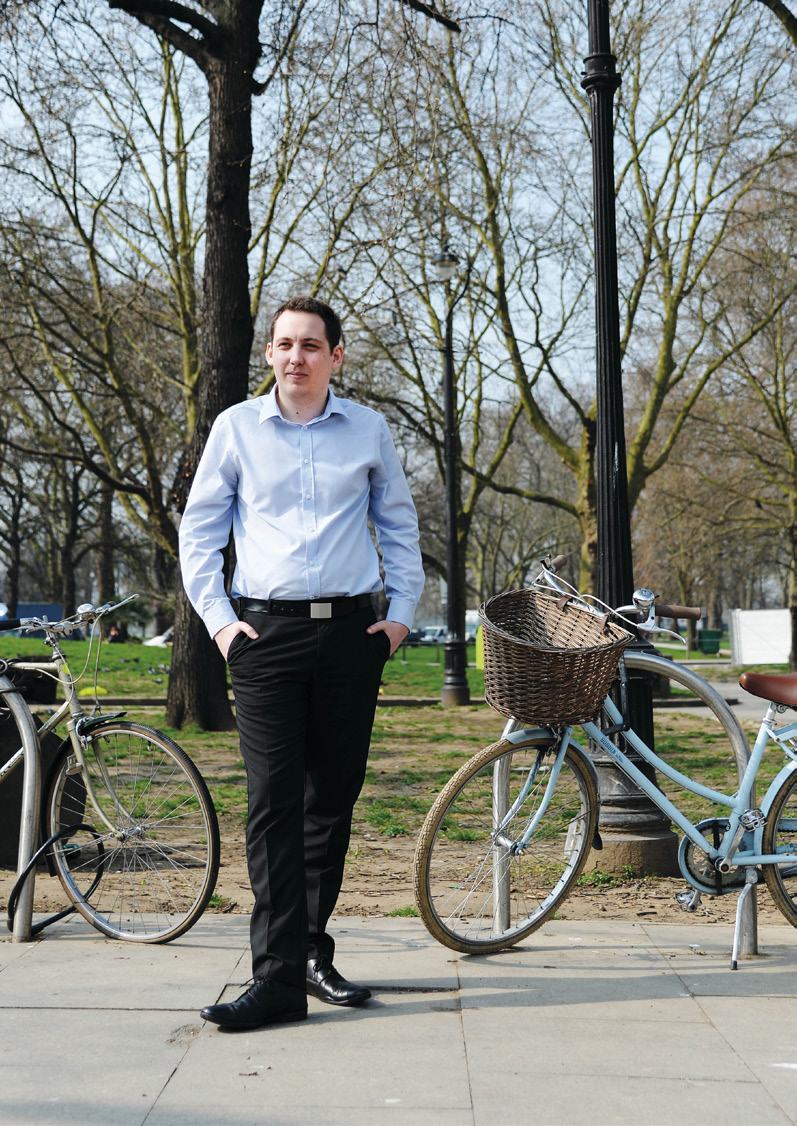 A man in a blue shirt and black pants standing outdoors between two bicycles on a paved path in a park.