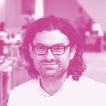 Portrait of a man with long dark curly hair and glasses, smiling.