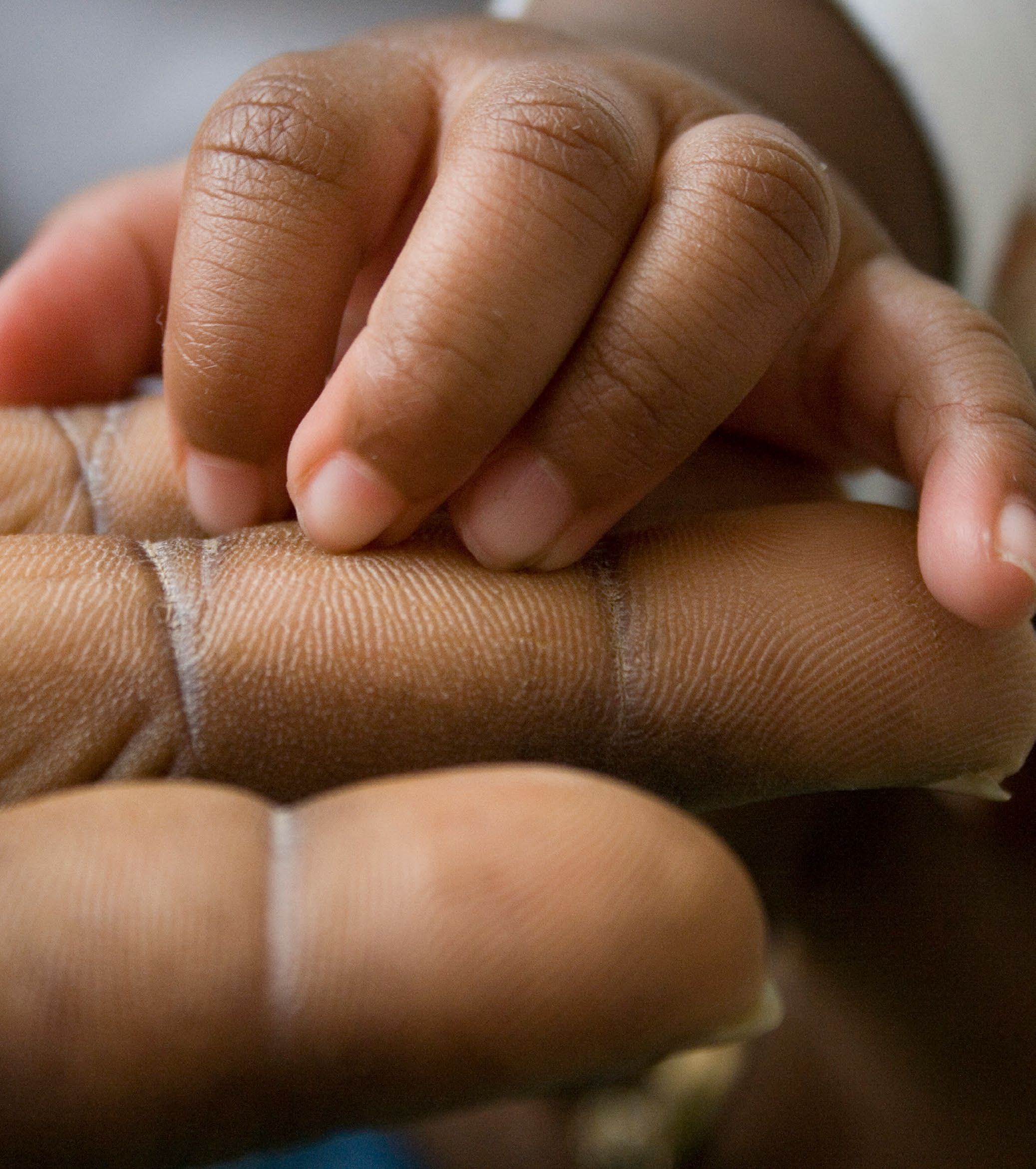 Close-up of an infant's small hand gently grasping an adult's finger.