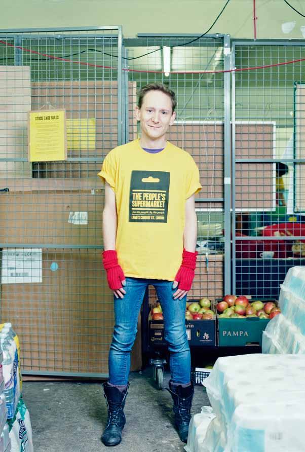 Man in a "The People's Supermarket" t-shirt stands in a supermarket storage area.