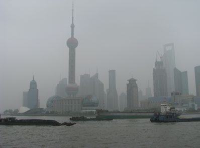 Hazy view of the Shanghai skyline with the Oriental Pearl TV Tower and other skyscrapers across a river with barges.
