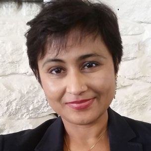Headshot of a woman with short dark hair and a nose piercing, smiling slightly.
