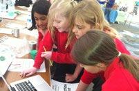 Four young girls in red shirts collaboratively engage with a laptop and papers, suggesting an educational or project-based activity.
