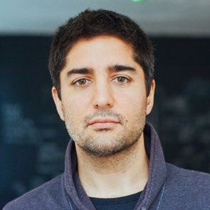 Headshot of a man with dark hair, brown eyes, and a beard, looking directly at the camera