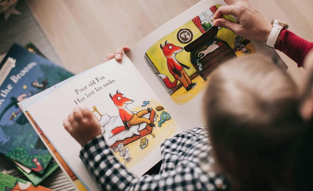An adult and child's hands point to illustrations of a fox looking for socks in an open children's book.