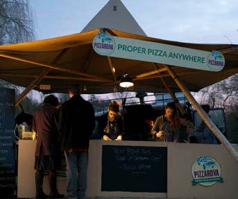 An outdoor "Pizzanova" food stall with a sign reading "Proper Pizza Anywhere", people working, and customers.