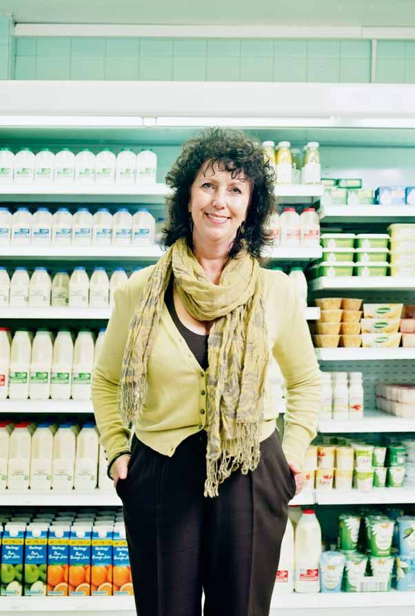 Woman with curly hair and a scarf smiles in front of a supermarket dairy aisle.