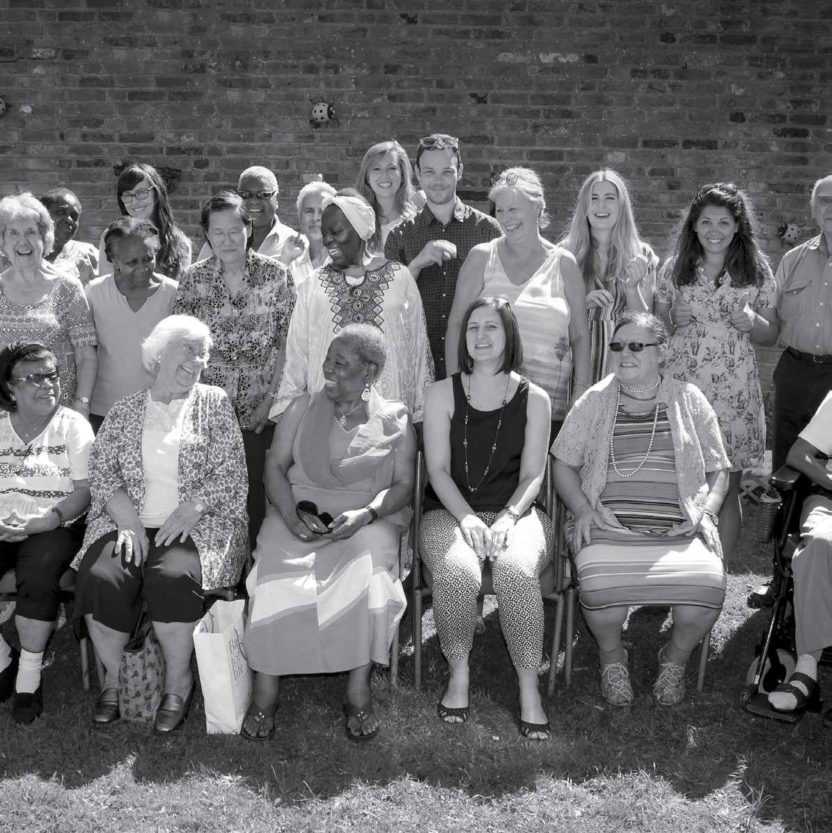 Black and white photograph of a diverse group of adults and seniors, smiling and posing outdoors in front of a brick wall.