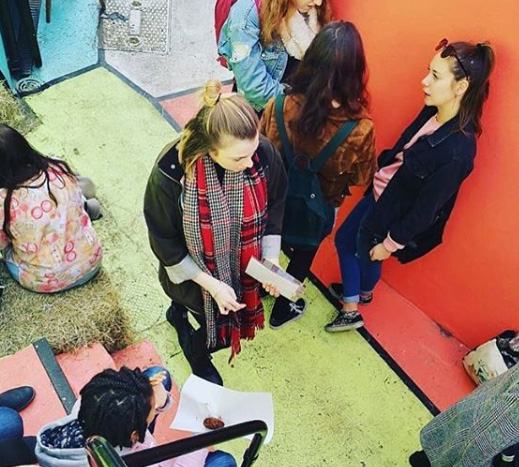 Group of young people interacting in a colorful outdoor setting, with one person showing something in a box.