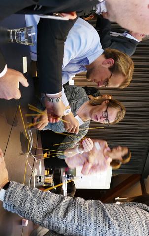 People at a table participate in a team-building exercise, using spaghetti to construct a structure.