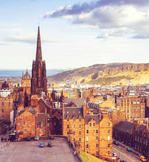 Aerial view of Edinburgh cityscape, featuring a prominent church spire amidst historic buildings and distant hills under a partly cloudy sky.