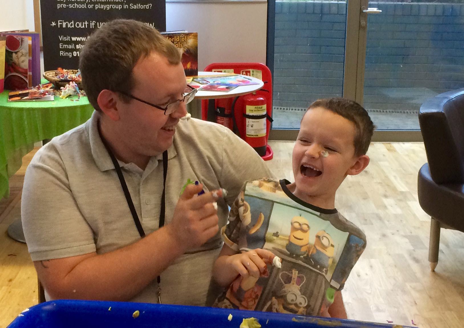 A man and a young boy laughing happily while looking at something on a table, illustrating positive human interaction.