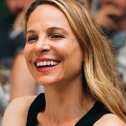 Close-up headshot of a smiling woman with long blonde hair, wearing a black top