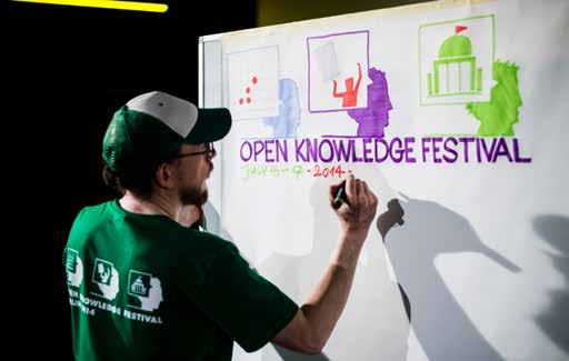 Person writing "OPEN KNOWLEDGE FESTIVAL JULY 15-17 - 2014-" on a whiteboard with colorful illustrative icons.