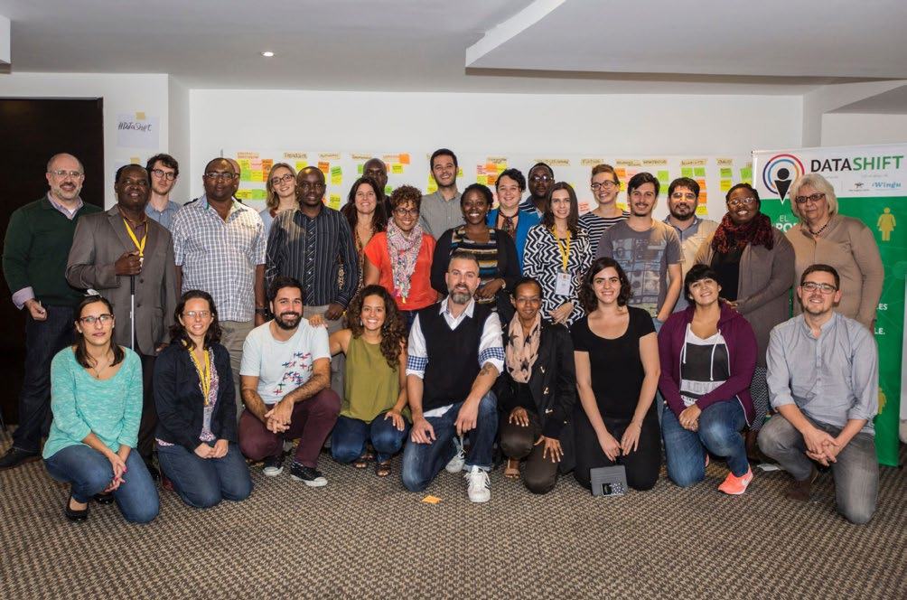 Large group of diverse people posing for a photo in front of a wall covered with sticky notes.