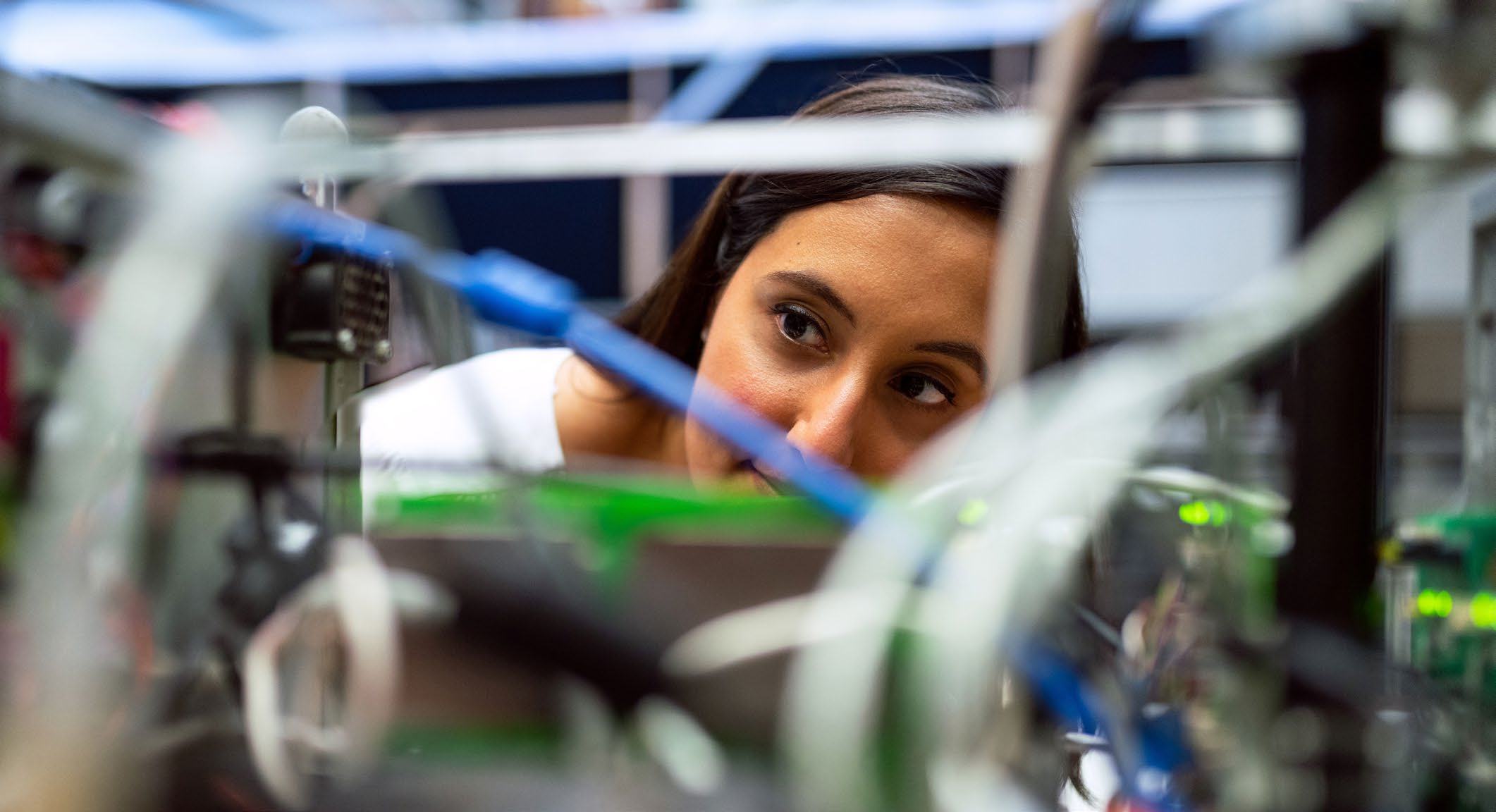 A woman with dark hair focuses on intricate electronic circuitry and components.