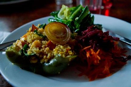 A close-up of a plate with a stuffed bell pepper filled with couscous, served with shredded carrots, beets, and greens.