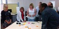 A group of people gathered around a table with sticky notes and markers, engaged in a collaborative brainstorming session in an office.