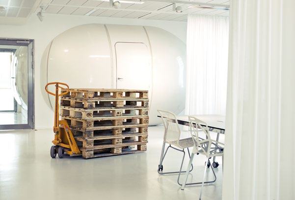 Modern office interior featuring a stack of pallets on a hand truck, an egg-shaped room, and a meeting table.