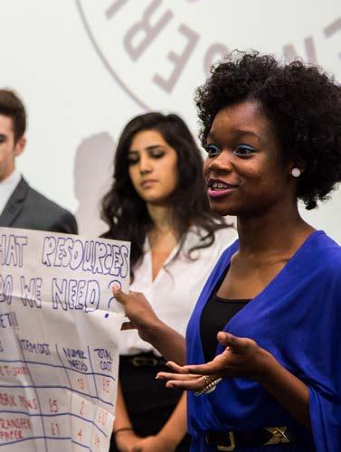 A young woman presents, holding a handwritten flip chart asking "WHAT RESOURCES DO WE NEED?" with a table for costs and items.
