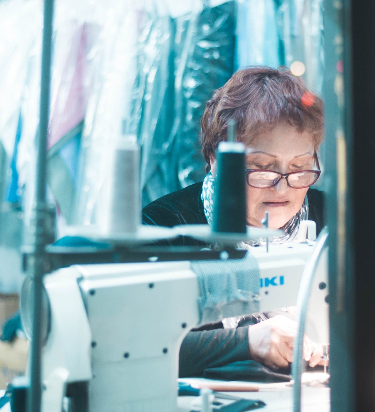 A woman with glasses focused on sewing fabric using an industrial sewing machine.