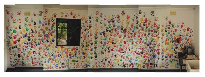 A white wall covered in numerous colorful handprints, with a dark window in the center.