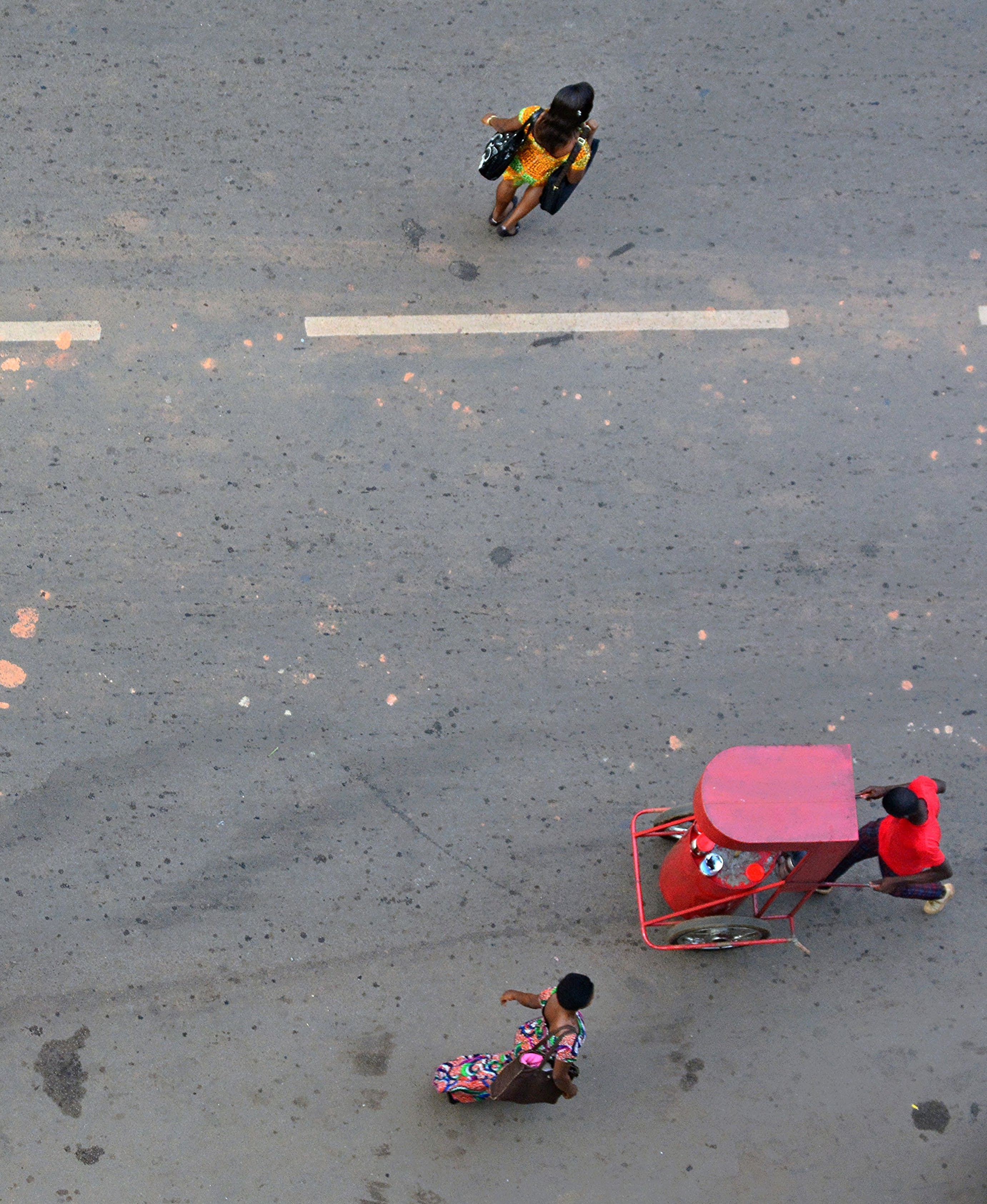 Aerial view of a street scene with two pedestrians and a red three-wheeled vehicle, possibly a rickshaw or cart.
