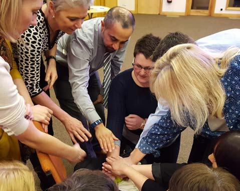 Group of diverse adults in a circle, stacking hands in a team-building exercise, emphasizing collaboration and unity.