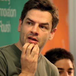 Close-up portrait of a man with dark hair, looking thoughtful, with a "Nesta: Making Innovation Flourish" banner in the background.