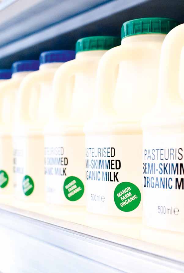 A row of "Manor Farm Organic Semi-Skimmed Milk" cartons with green caps and labels on a supermarket shelf.